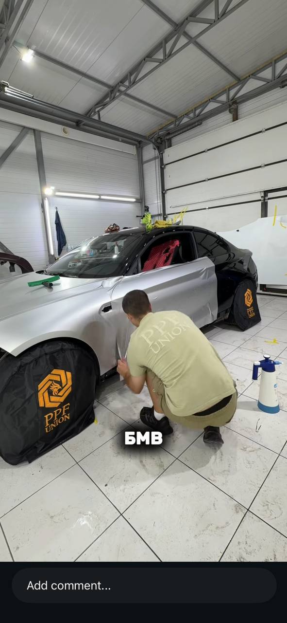 Мастер оклеивает дверь BMW серебристой плёнкой в мастерской